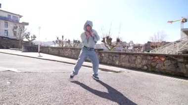 Kendinden emin genç erkek dansçı güneşli şehir caddesinde dinamik serbest hareketler sergiliyor, kişisel stil ve tutkusunu enerjik hareketlerle ifade ediyor.