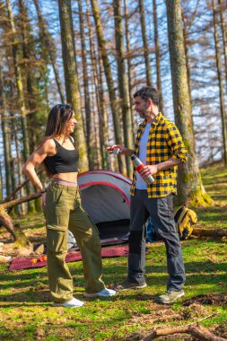 Yürüyüşçüler yemyeşil bir ormandaki kamp alanlarında sıcak içeceklerin tadını çıkarıyorlar, doğanın ortasında bir rahatlama anını paylaşıyorlar.