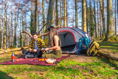 Yürüyüşçüler ormanda kamp yaparken çadırlarının önünde kağıt oynayıp atıştırmalık yerler.