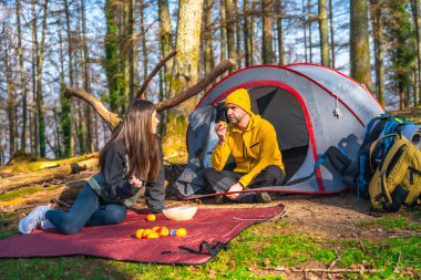 Birkaç yürüyüşçü ormanda kamp yaparken çadırlarının yanında atıştırıyor, güneşli havanın tadını çıkarıyorlar.