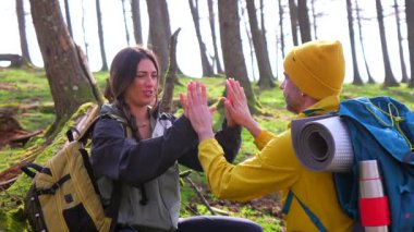 Sırt çantalı gezginler orman molasında patty cake oynuyorlar, neşeli anları ve arkadaşlıkları paylaşıyorlar parlak güneş ışığı altında.