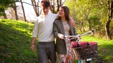 Romantik çift bisikletleriyle parkta rahatça yürüyüp özel bir anı paylaşıyorlar.