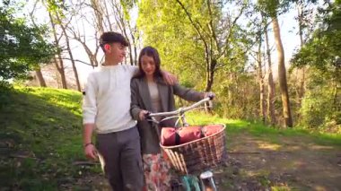 Romantik çift bisikletleriyle parkta rahatça yürüyüp, birlikte hassas bir anı paylaşıyorlar.