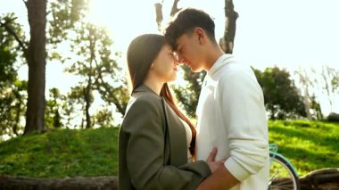 Romantik çift, güneşli yeşillikler arasında samimi bir kucaklaşmayı paylaşıyor. Yumuşak bir bağ ve birlikte huzurlu bir park kurma anı.