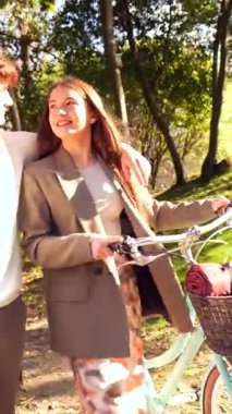 Sevgi dolu çift pedal çeviriyor ve manzaralı park yolunda yürüyor, yemyeşil yemyeşil bir günde güneşli bir anı paylaşıyor.
