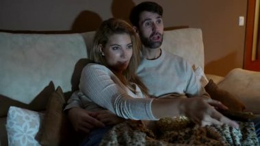 Evde romantik bir akşam, bir çift kanepede patlamış mısırla film gecesinin tadını çıkarıyor, kahkahalarını ve hassas anlarını paylaşıyor.