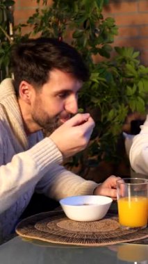 Genç çift balkonlarında kahvaltı yapıyor, mısır gevreği yiyor, portakal suyu içiyor ve konuşuyor.