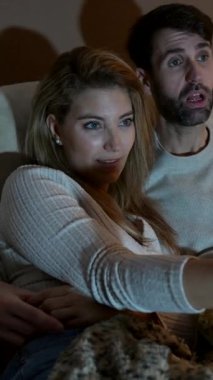 Romantik partnerler yumuşak battaniyenin altında sarılıp patlamış mısırlarını paylaşırken sıcak bir ev ortamında film izlemenin keyfini çıkarıyorlar.