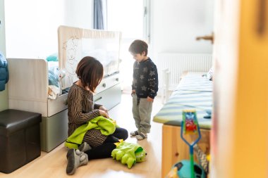 Anne ve oğlu evde birlikte oynuyorlar, yatak odalarında oyun oynamak için dinozor kostümü hazırlıyorlar.