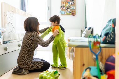 Anne oğluna dinazor kostümü giydiriyor, rahat bir yatak odasında, neşeli anları paylaşıyor ve birlikte uzun süreli anılar yaratıyor.