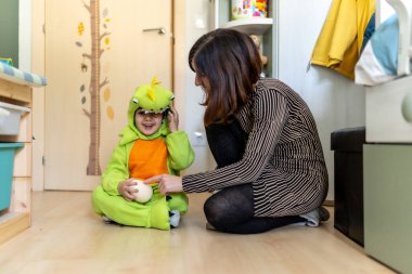 Anne ve oğlu birlikte eğleniyor, dinozor kostümü ve bir çocuğun yatak odasında yumurta ile oynuyorlar.
