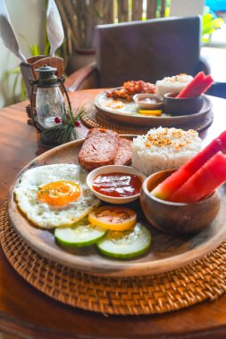 Pirinç, kızarmış yumurta, öğle yemeği eti, karpuz, domates, salatalık ve sos içeren lezzetli filipino kahvaltısı Siargao Adası 'ndaki ahşap bir tabakta servis edilir.