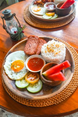 Siargao adasındaki ahşap bir tabakta spam, pilav, sahanda yumurta, taze meyve ve sebzelerin yer aldığı canlı filipino kahvaltı tabağının tadını çıkarıyorum.