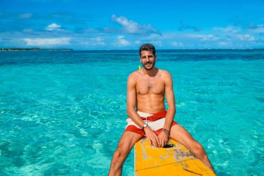 Sarı banka teknesinde dinlenen genç adam Daku Adası, Siargao, Filipinler 'in turkuaz tropikal denizinde yaz tatilinin tadını çıkarıyor.