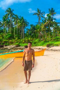 Genç adam yaz tatilinin tadını çıkarıyor, Kawhagan adasında tropikal bir sahilde yürüyor, siargao, Filipinler