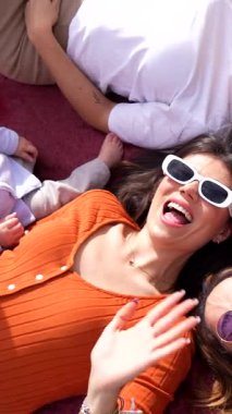 Bir grup neşeli çoklu etnik arkadaş battaniyeye uzanıp komik jestler yapıyor, gülümsüyor ve eğleniyorlar.