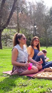 Aileler ve arkadaşlar güneşli bir parkta hoş bir pizza pikniği için toplanıyor, kahkahaları paylaşıyor ve birlikte güzel anılar yaratıyorlar.