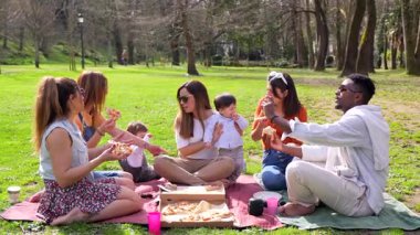 Çok kültürlü bir aile parkta piknikte pizza yiyerek eğleniyor, iyi vakit geçiriyor ve birlikte gülüyorlar.