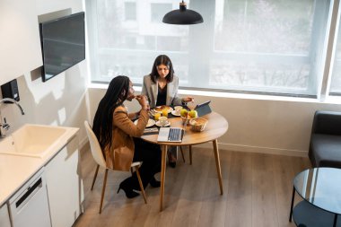 İki iş kadını iş gezisi sırasında bir tablet ve dizüstü bilgisayar üzerinde çalışırken otel odalarında kahvaltı yapıyorlar.