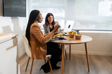 İki iş kadını bir iş gezisi sırasında otel odalarında laptopla kahvaltı yapıyor.