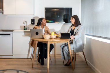 İki iş kadını kahvaltıdan zevk alıyor ve bir iş gezisi sırasında bir otel odasında dizüstü bilgisayar ve tabletle çalışıyor.