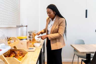 İş kadını, iş gezisi sırasında otel büfesinde kahvaltısını yaparken yoğurduna şeker ekliyor.