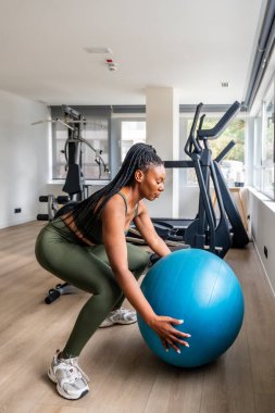 İş kadını seyahat ederken rutinini sürdürüyor, bir otel spor salonunda spor topu ile çömelme hareketleri yapıyor.