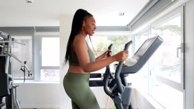İş gezisi sırasında otel fitness salonunda eliptik çapraz antrenör üzerinde egzersiz yapan siyahi iş kadını.