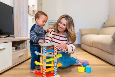 Anne ve çocuk birlikte oyun oynuyorlar, rahat oturma odalarında renkli bir oyuncak araba rayı ile meşgul oluyorlar.