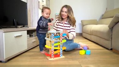 Sevgi dolu anne, oyuncak bebek bebekle ahşap bir rampa kullanıyor, rahat oturma odasında neşeli anlar paylaşıyor.