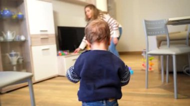 Anne yeni yürümeye başlamış oğlunun yanına çömelmiş oyuncak mutfakla şakalaşıyor ve sıcak oturma odasında oturup kaliteli bir bağ kurma anını paylaşıyor.