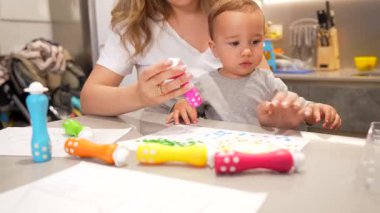 Anne ve küçük çocuk yaratıcı oyun zamanlarının keyfini çıkarıyorlar. Mutfaklarında renkli noktalı kalemlerle resim yapıyorlar.