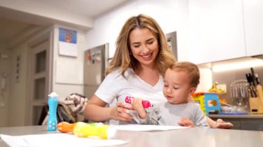 Yaratıcılığı oyuncu sanatlarla beslemek, ilgili bir anne, bebeğini canlı kalemlerle çizerken, mutfak masasında birlikte otururken rehberlik etmek.