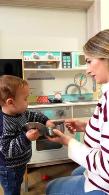 Genç anne, küçük oğluna oyuncak mutfağıyla oynaması için yardım ediyor. Erken çocukluk gelişimini ve yaratıcı oyunlarını teşvik ediyor.