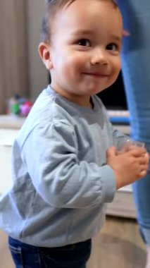 Bebecik bağımsız içmeyi öğreniyor, mutfakta su bardağında ustalaşırken çeşitli ifadeler gösteriyor, çocukluğun gelişimsel dönüm noktasını neşeli hareketlerle gösteriyor