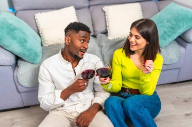 Oturma odasında şarap kadehleriyle oturmuş birlikte rahat bir anın tadını çıkaran gülümseyen bir çift.