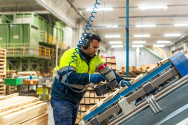 Bir geri dönüşüm fabrikasında paletleri yeniden kullanmak için düzenleyen beyaz bir işçinin üç çeyrek boy fotoğrafı.