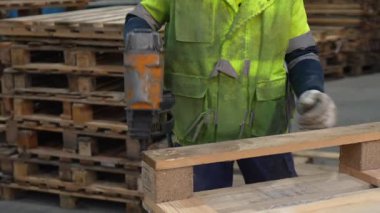 İşçi, geri dönüşüm tesisinde pnömatik çivi tabancasıyla ahşap paletler birleştiriyor. Etkili marangozluk teknikleri sergiliyor.