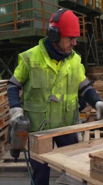 Yetenekli marangoz ahşap paletleri geri dönüşüm tesisinde monte etmek için pnömatik çivi tabancası kullanır ve verimli ahşap işçiliği teknikleri gösterir.