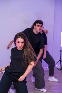 Bir grup genç dansçı, mor neon ışıkları olan bir dans stüdyosunda modern bir koreografi uyguluyorlar.