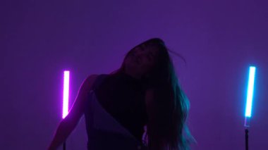 Enerjik dansçı, canlı mor ve mavi renkli tüp ışıklarının altında hareketli ve büyüleyici bir performans sergiliyor.