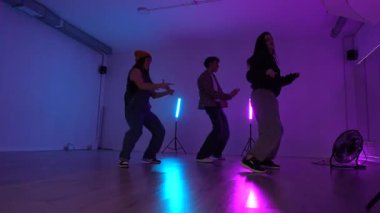 Bir dans stüdyosunda modern bir koreografi uygulayan bir grup genç dansçı neon ışıklarıyla aydınlatılmış.