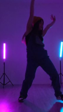 Enerjik dans öğrencisi hareketlerini renkli neon ışıklarla aydınlatılmış canlı bir stüdyoda yapıyor.