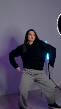 Bir dans stüdyosundaki renkli ışıklar altında dinamik hareketler yapan enerjik bayan dansçı tutkusunu ve yeteneğini sergiliyor.