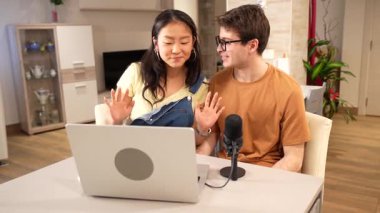 Podcast 'te birlikte çalışan, dizüstü bilgisayar ve mikrofonla evde oturan, işbirlikçi dijital içerik oluşturma işine giren çok ırklı genç bir çift.