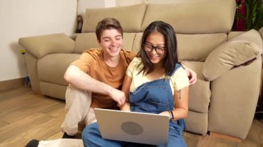 Genç, çok ırklı bir çift, özel dijital anı paylaşıyor, dizüstü bilgisayarlarında birlikte internete girip rahat bir şekilde evlerinde oturuyor, gerçek bir bağ ve neşe ifade ediyorlar.