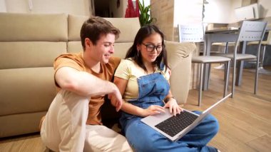 Dizüstü bilgisayarda birlikte çalışan çok ırklı çift, rahat ev ortamında dijital alanı neşe ve bağlantıyla paylaşıyor, modern işbirlikçi yaşam tarzını sergiliyor