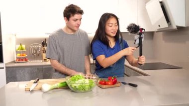 Mutlu çok ırklı çift birlikte sağlıklı bir salata hazırlıyor ve modern bir mutfakta video kaydediyor.