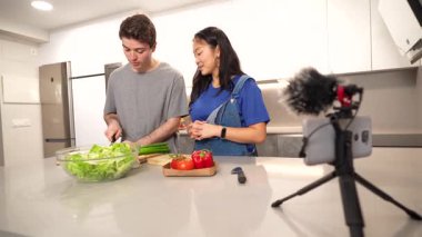 Modern bir mutfakta birlikte sağlıklı bir salata hazırlayan çok ırklı çift video blogları için mutfak maceralarını kaydediyor.