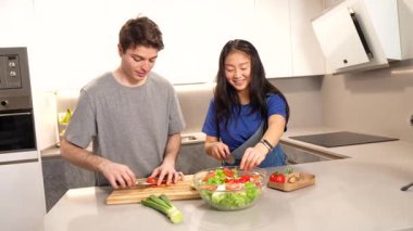 Birlikte çalışan çok ırklı bir çift taze sebze doğrayıp besleyici salata hazırlarken aynı zamanda lüks mutfak ortamında sıcak anları paylaşıyorlar.